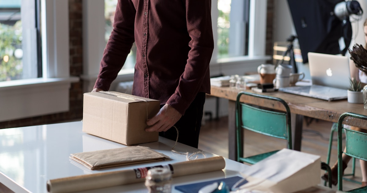Person holding a cardboard box at a packing table in a small online store